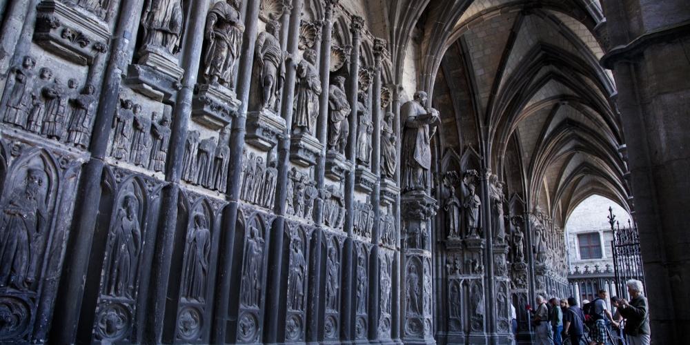 L'entrée de la Place de l'Evêché est précédée d'un porche gothique du XIVe siècle orné de sculptures de diverses époques, parmi lesquelles figurent des figures de prophètes et une sculpture de la Vierge, patronne de la cathédrale. – © Jan D'Hondt / VisitWapi