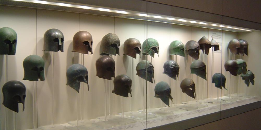 The range of valuable finds includes a display case with a collection of finely preserved bronze helmets of the Archaic-Classical periods. – © Hellenic Ministry of Culture and Sports / Ephorate of Antiquities of Ilia