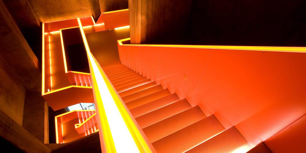 The stairwell in the coking coal bunker’s nearly 20-metre-deep shaft takes visitors to the Ruhr Museum’s exhibition levels. The orange colour marks a newly introduced element. – © Thomas Willemsen / Zollverein Foundation