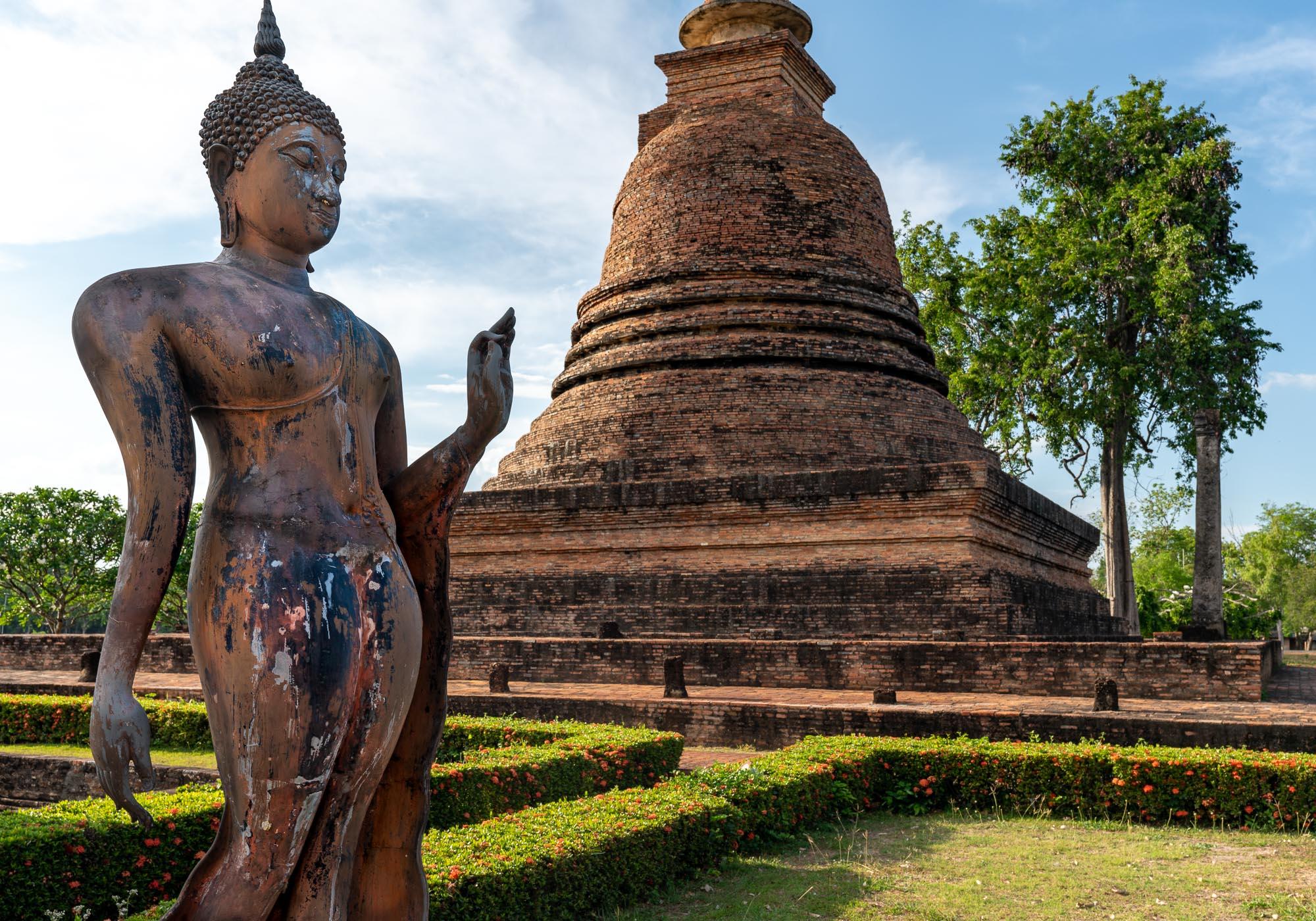 A statue in the Sukhothai style alongside the central stupa of Wat Sa Si on an island in a reservoir. – © Michael Turtle