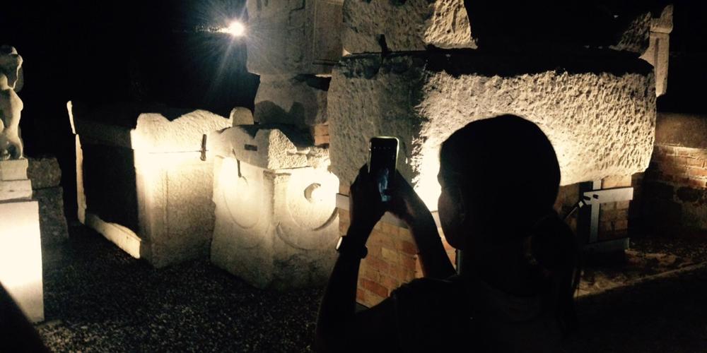 A young visitor capturing architectural details during her night visit to the necropolis. – © Erica Zanon