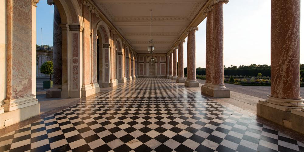 Le Grand Trianon est érigé par Jules Hardouin-Mansart en 1687, suite à la demande de Louis XIV qui souhaite un endroit pour s'éloigner de la pompe de la cour et pour poursuivre sa liaison avec Mme de Montespan. Ce petit palais tout de marbre rose et de porphyre est peut-être l'ensemble architectural le plus raffiné du domaine royal de Versailles. – © Thomas Garnier