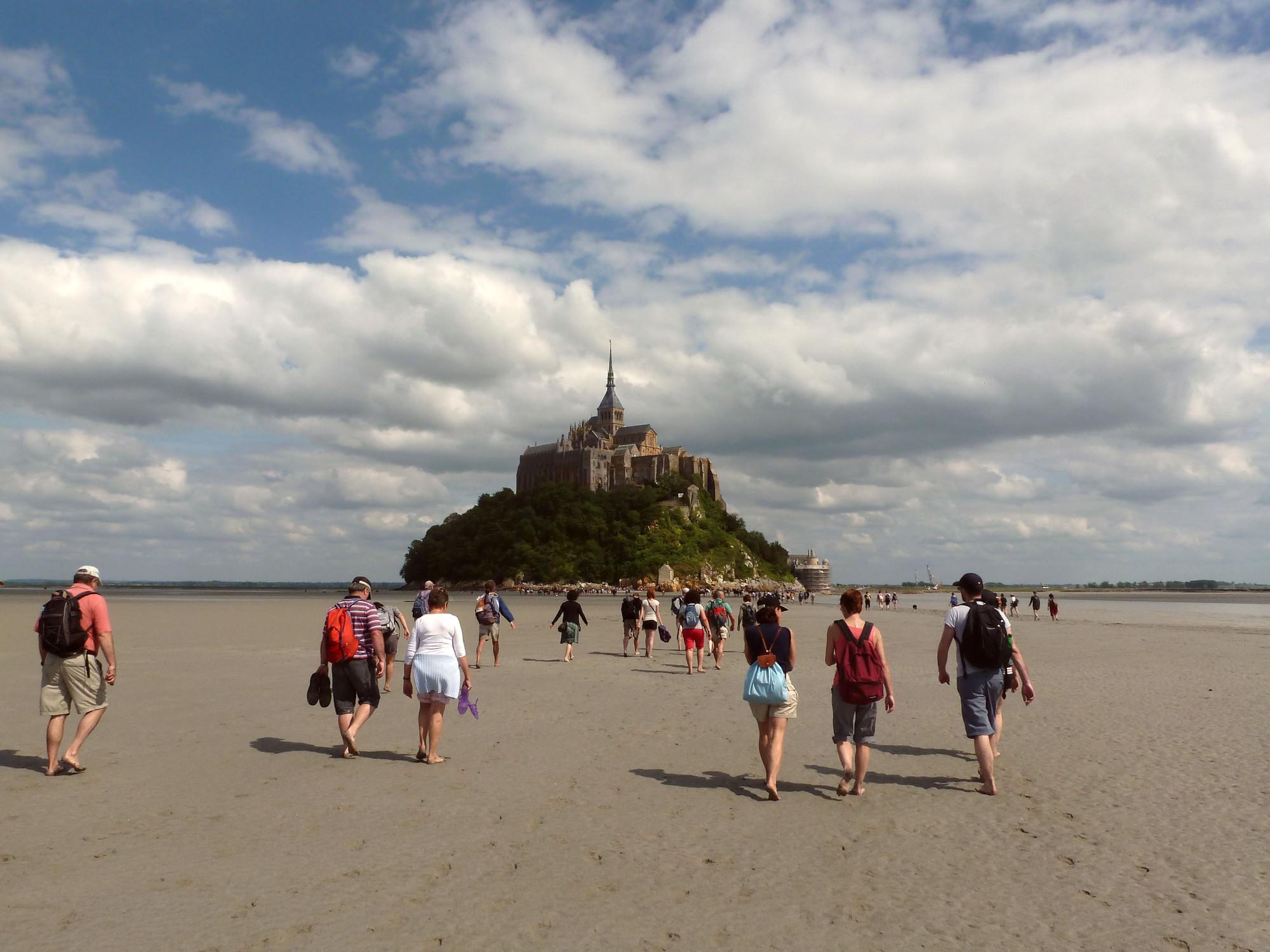 Accompanied by an experienced guide, visitors walk across the Bay of Mont-Saint-Michel, along a stretch of silvery sand, and over the meandering coastal rivers. – © K. Riley / CRT Normandie