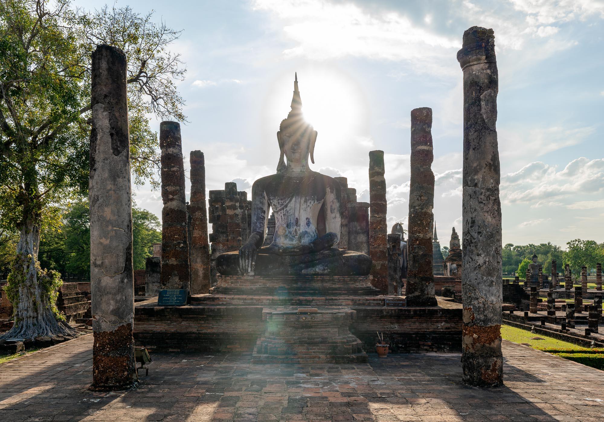 One of the important Buddha statues along the main axis of Wat Mahathat, with the sun setting in the background. – © Michael Turtle
