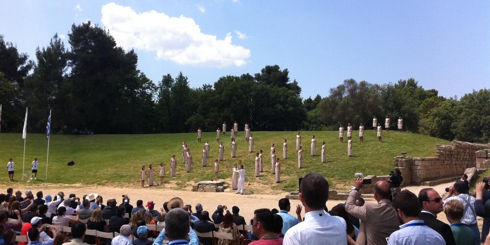 The Head Priestess passes the flame to the first torchbearer and the Torch Relay begins. – © Hellenic Ministry of Culture and Sports / Ephorate of Antiquities of Ilia