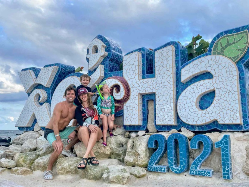 family in front of Xel-Ha sign ocean in background