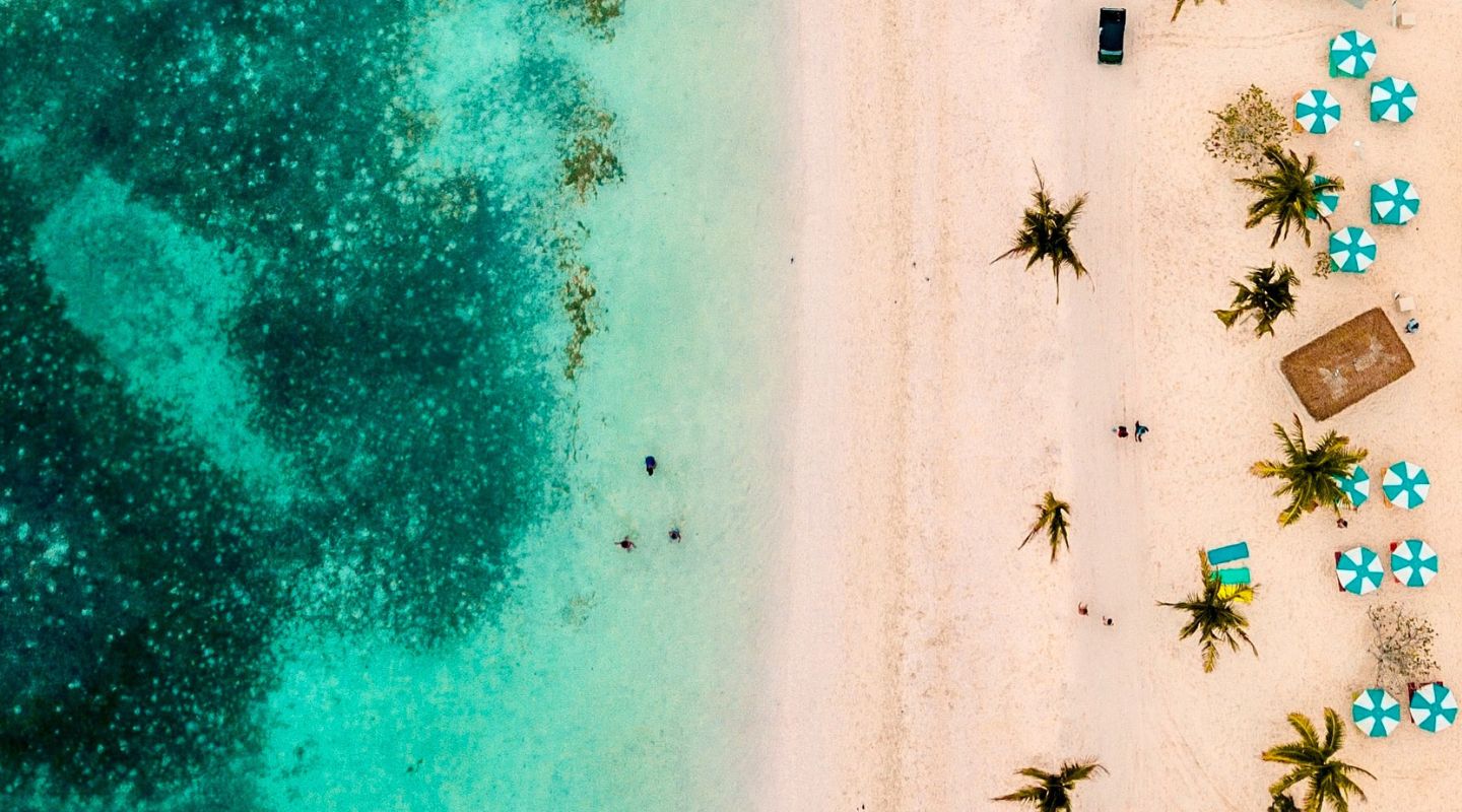 Drone view of the beach, with the ocean on one side and the beach on the other. Beach umbrellas and chairs can be seen in the picture. 