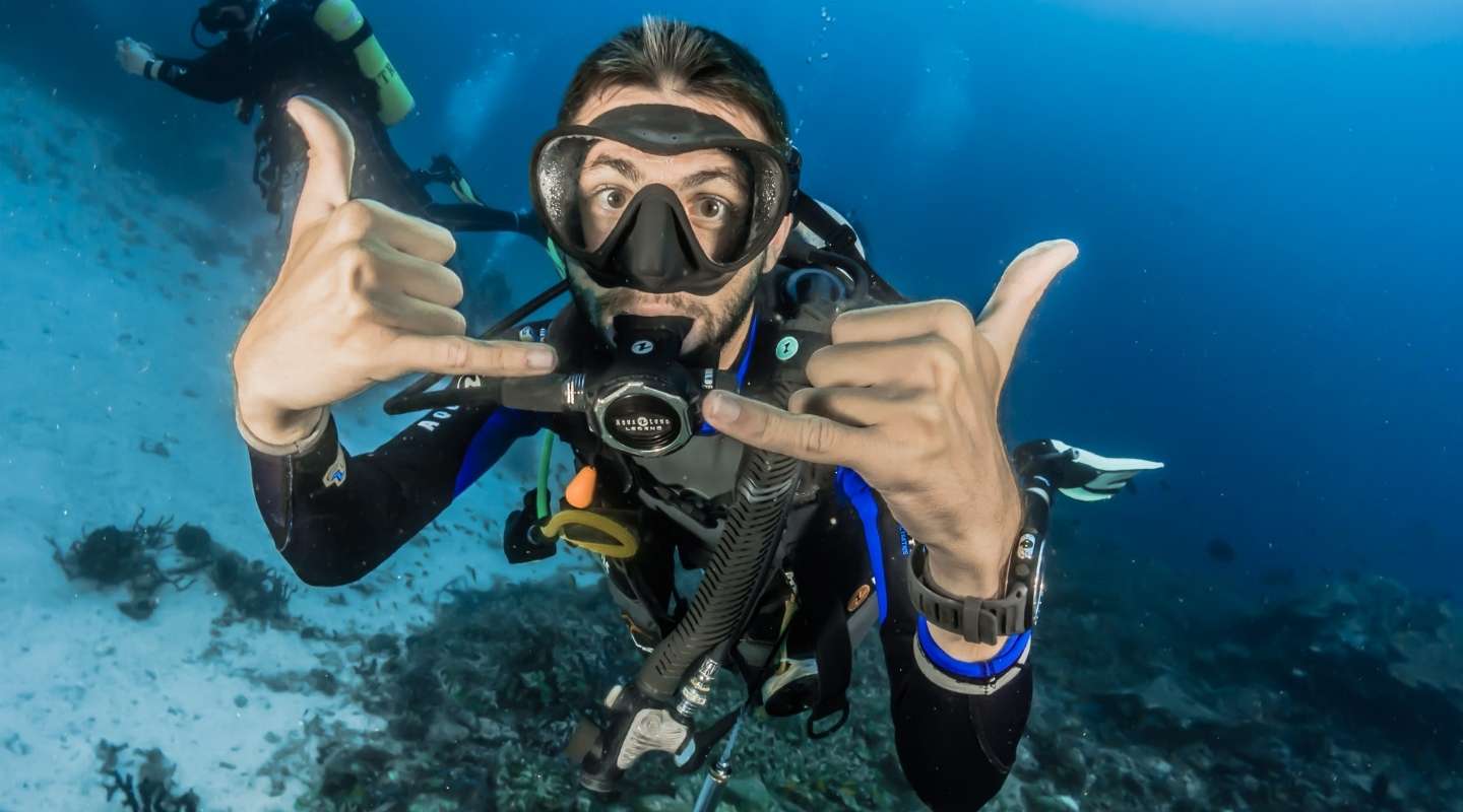 Man making a friendly sign with two hands while diving. 