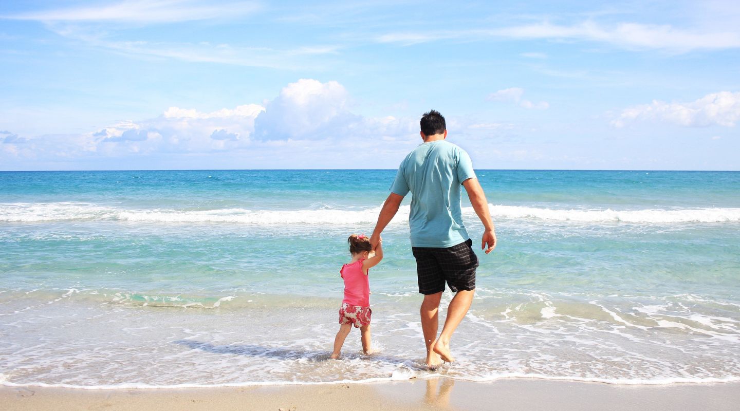 A man walks by the ocean hand in hand with a little girl