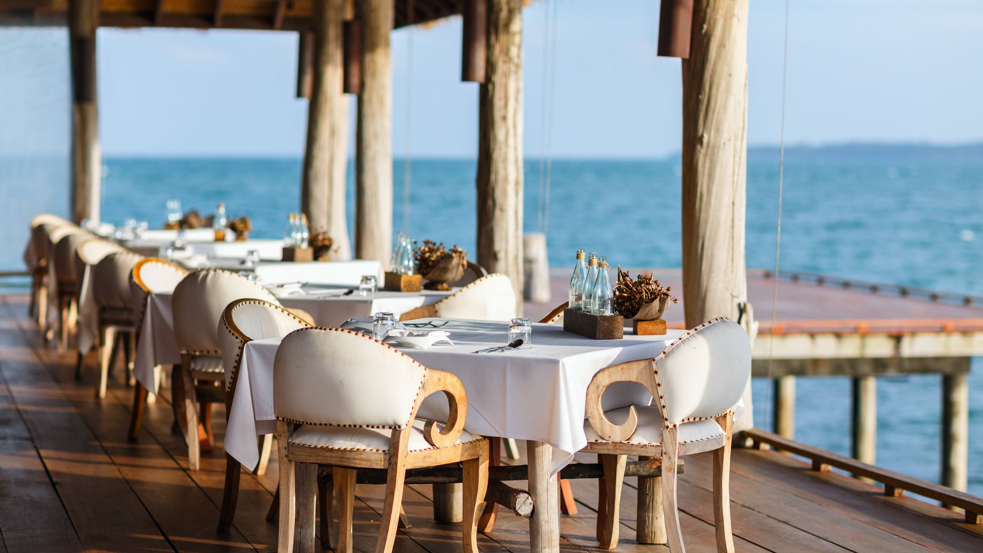 A group of tables with white seats with the ocean in the background