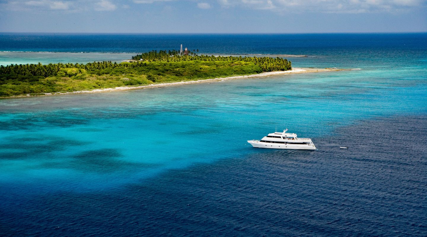 Side view of a white boat sailing towards the blue hole, with half of the water in the shot being a light blue and the other half being a dark blue.