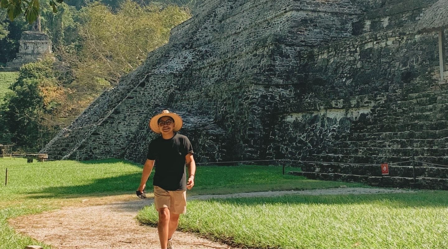 A man wearing a black shirt walks next to Mayan ruins