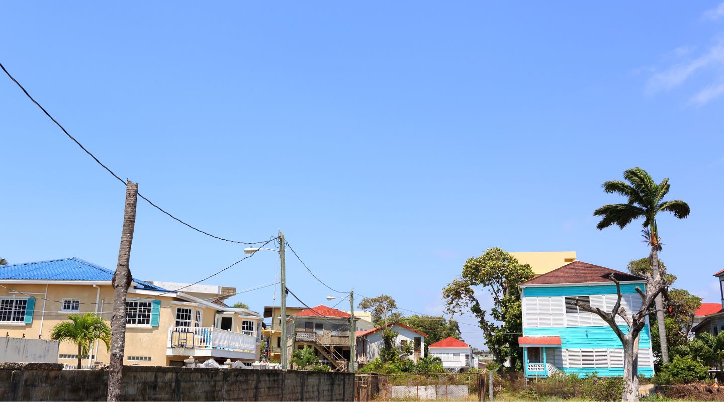 Street view of a couple of houses in Belize, painted in colorful colors, with sturdy fences surrounding them. 