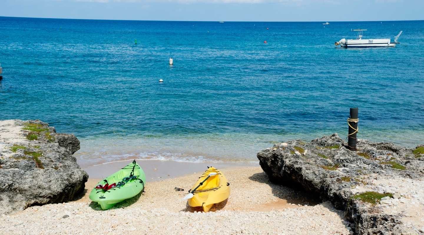 Two kayaks on the shore, overlooking the ocean and a small boat. 