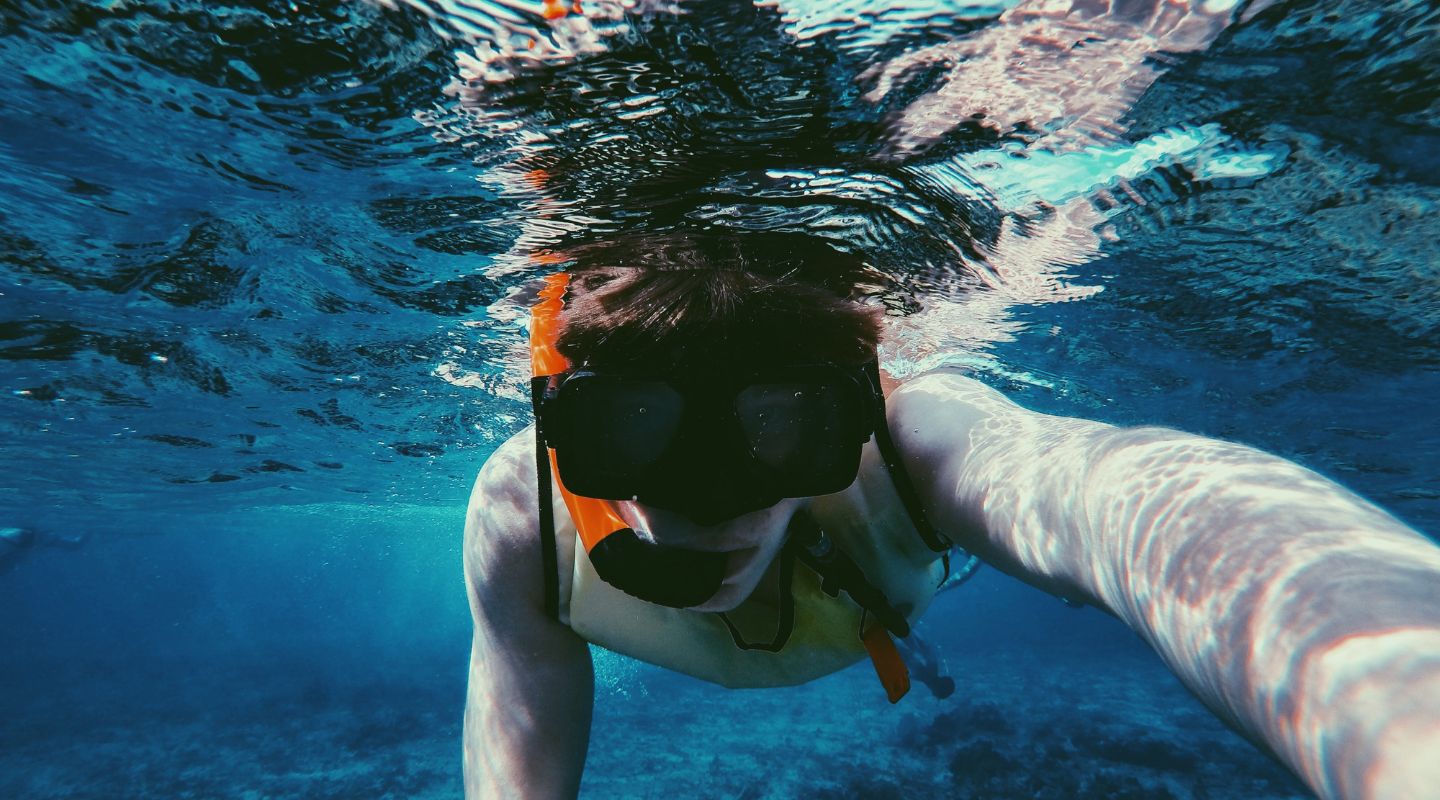 Young man holding a camera underwater and looking at it. 