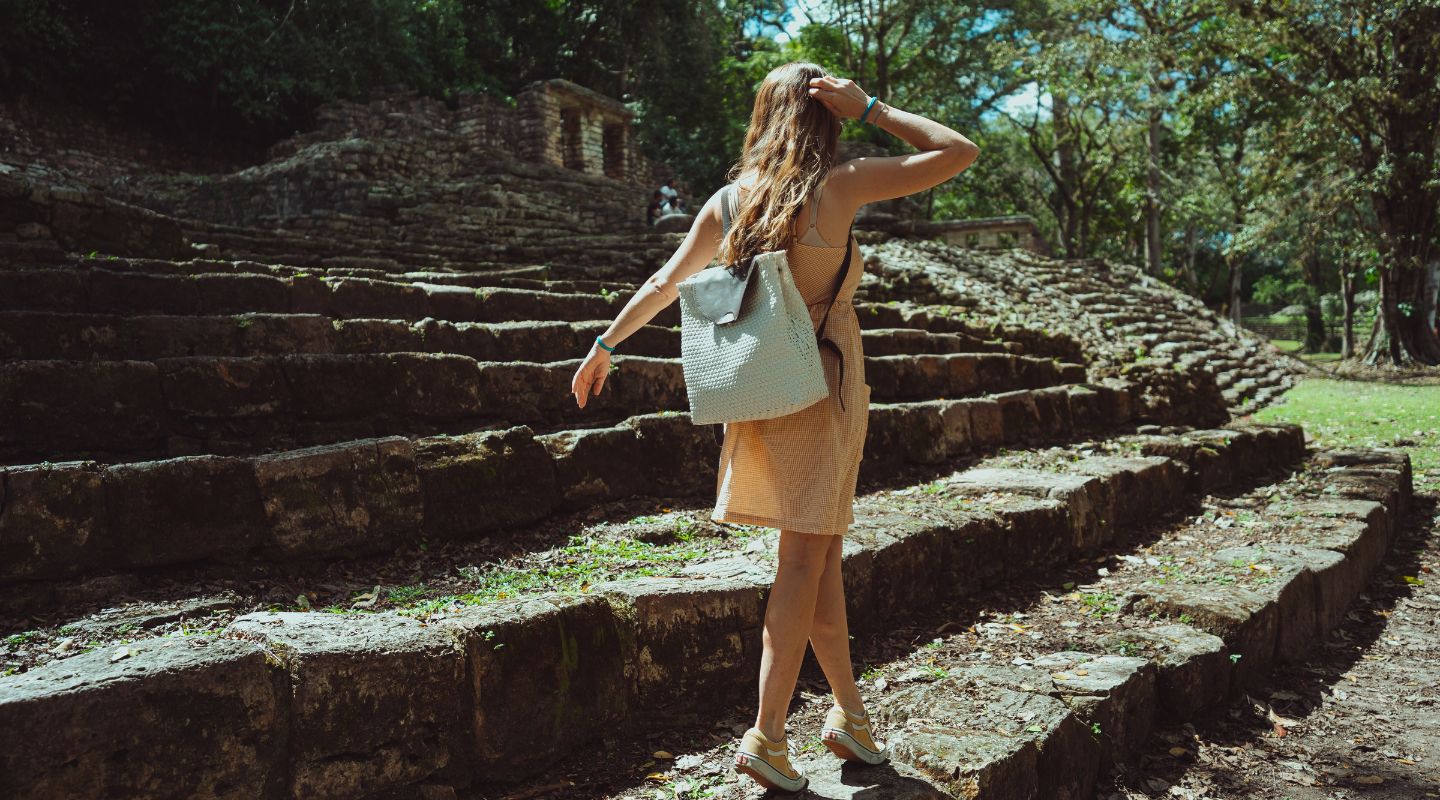 A woman dressed for hot weater walks on the ruined stairs of a Mayan archeological site