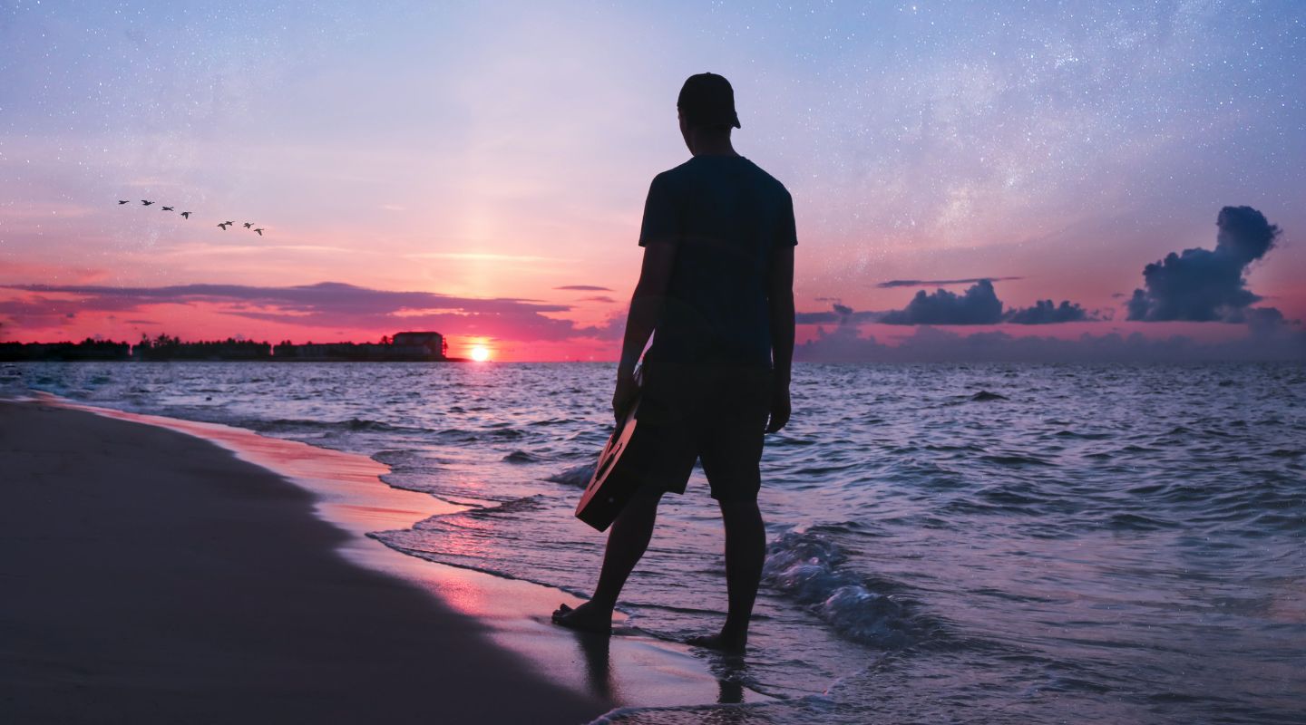 Man looking at the sunset, standing by the shore. 