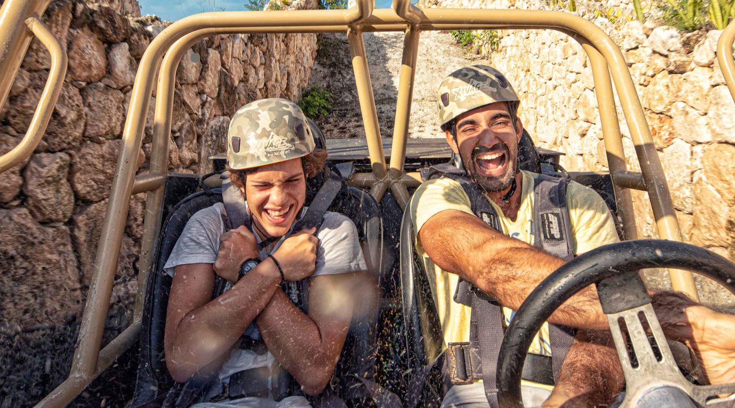 Two men covered in mud driving an ATV