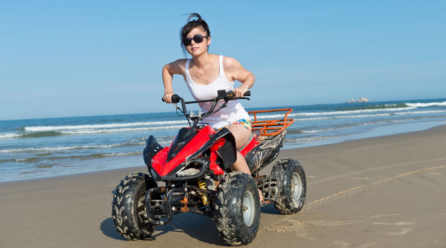 Woman driving a red ATV by the beach