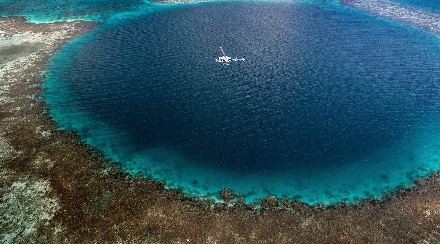 Aereal photo of the blue hole, with a catamaran floating on top of it.