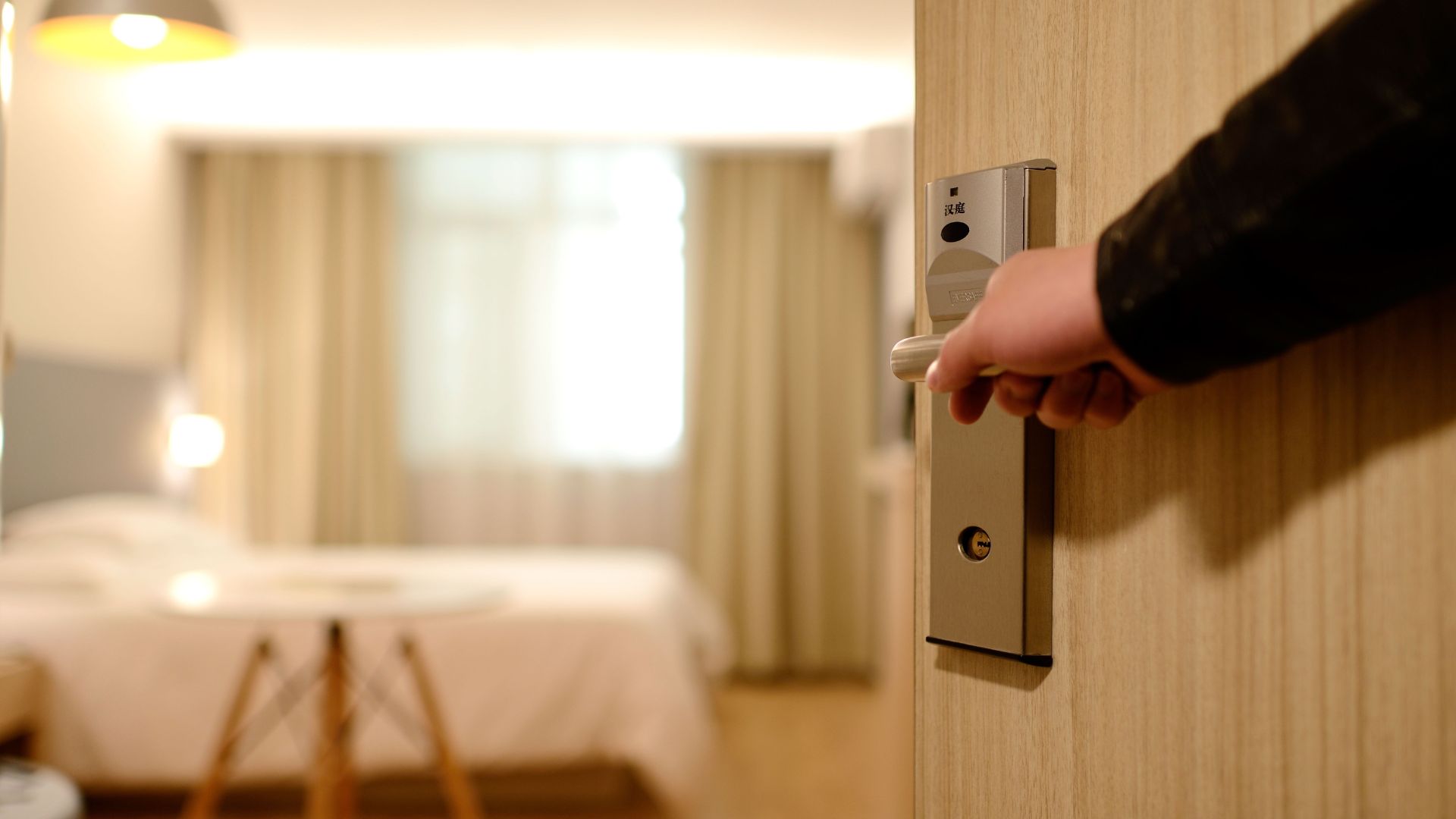 An arm opening a hotel bedroom's door revealing the interior