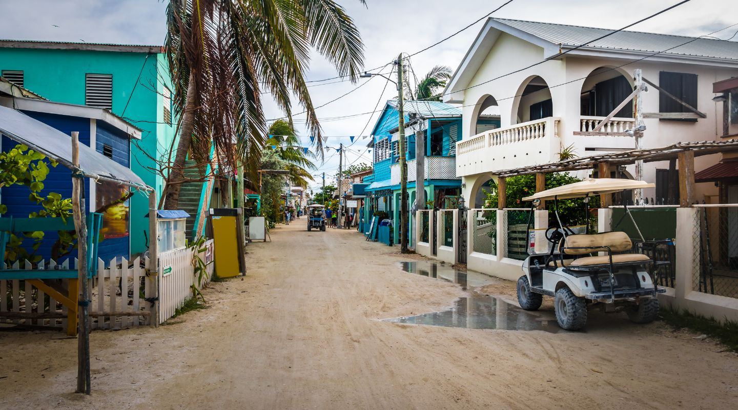 Small unpaved street between two rows of colorful buildings, with a golf cart parked outside of a house. 