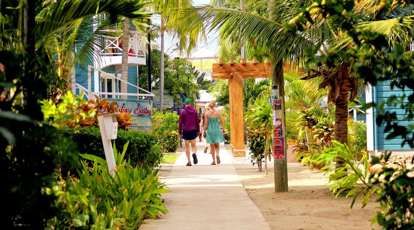 A couple walks down the street, with colorful houses and buildings surrounding them. 