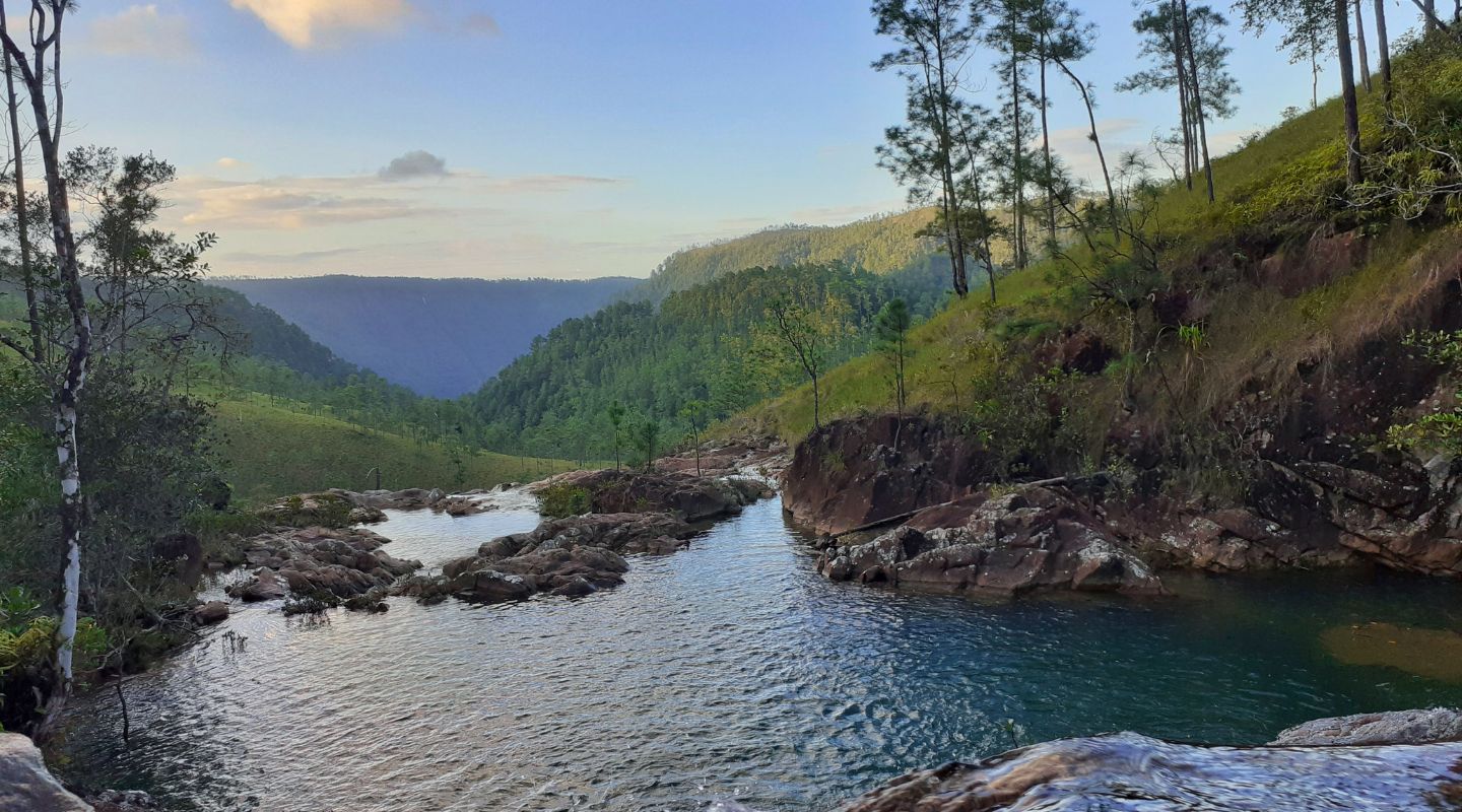 View of a lake in the mountains, leading to an unseen small waterfall