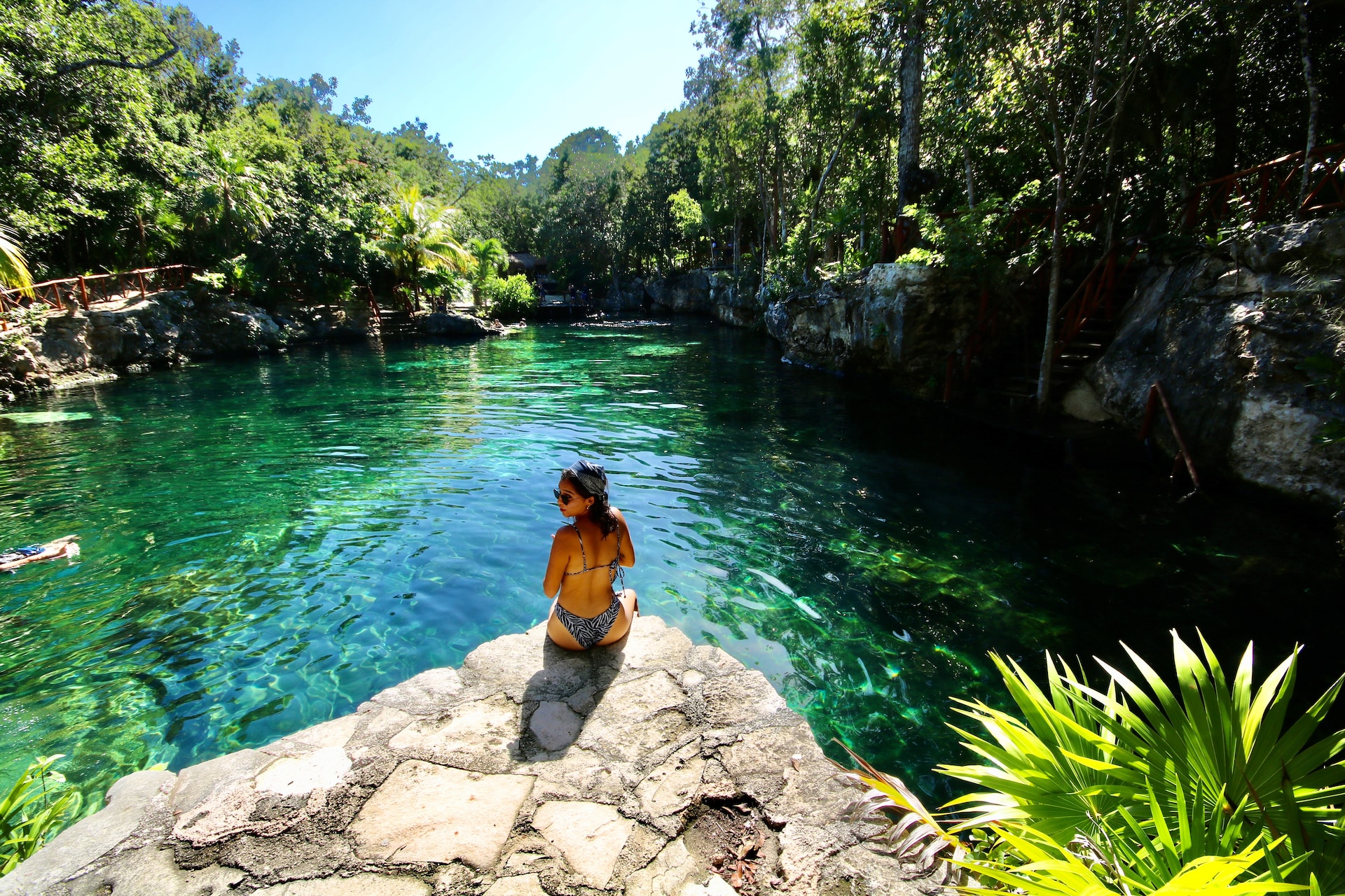 Woman in bathing suit sitting on a rock near a cenote.