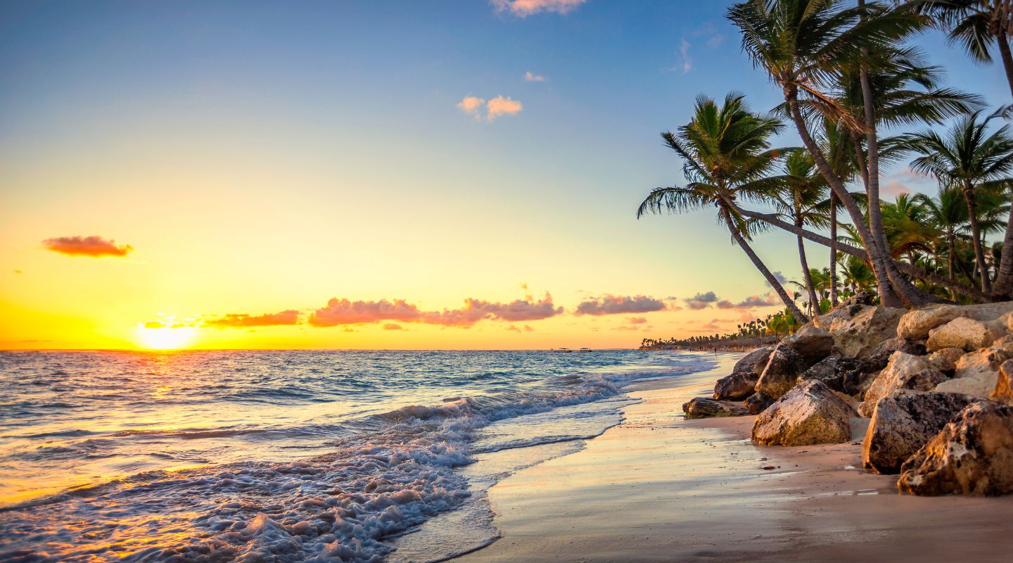 Photo of the beach at sunset, with beach loungers and parasols on one side, and the ocean on the other. 