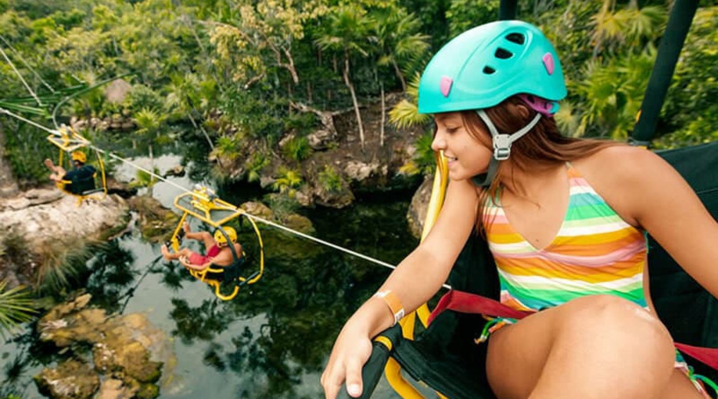 A woman sitting on a hammock of sorts looks down at a river and other travelers who are doing the same