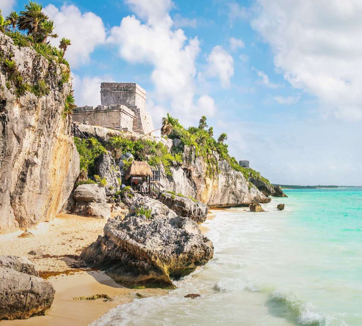 Tulum ruins sit high on a cliff overlooking a beach on a beautiful day. 