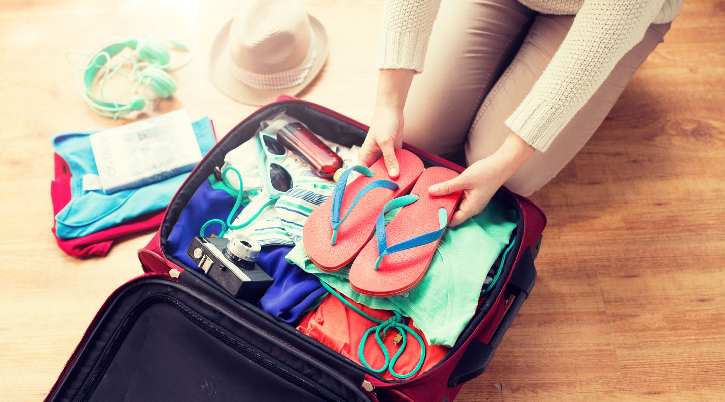 A woman packs sandals into a suitcase.