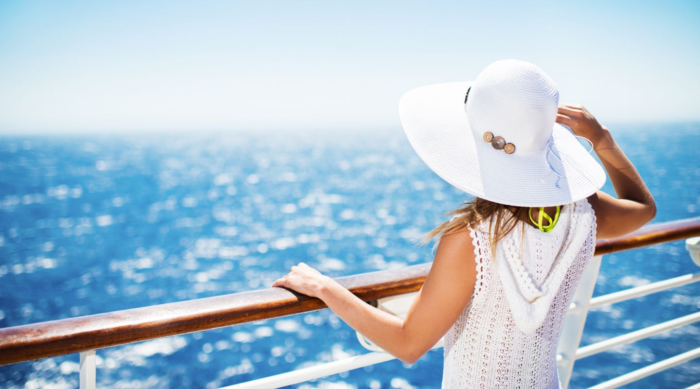 A woman dressed in white stands on a cruise deck while overlooking the ocean