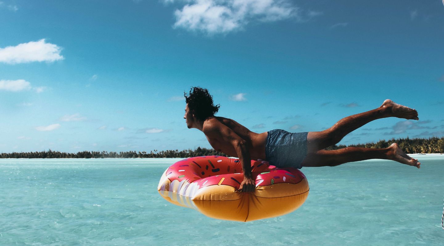 Man holding an inflatable donut and jumping into the ocean.