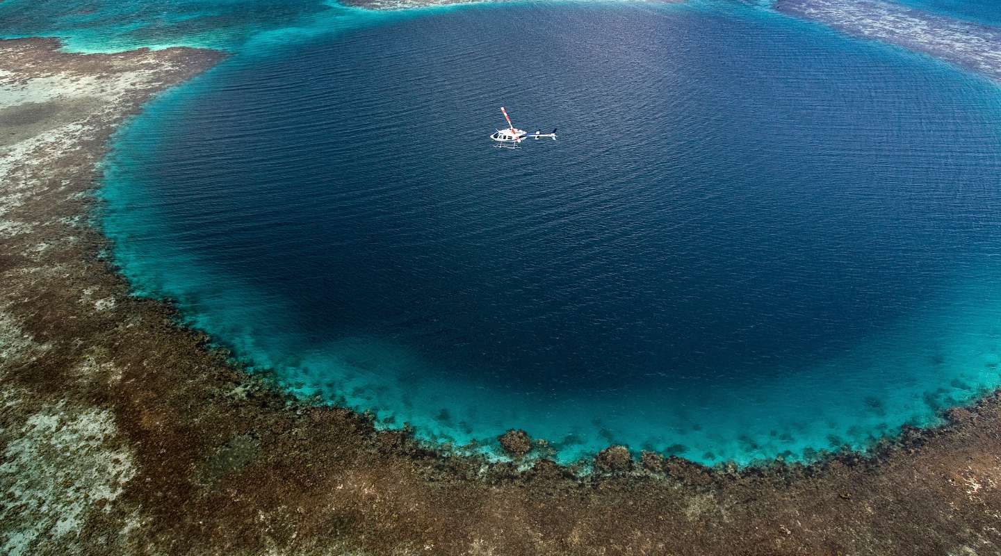 Aereal view of Belize's Blue Hole, with a boat shown in the middle to show the hole's scale.