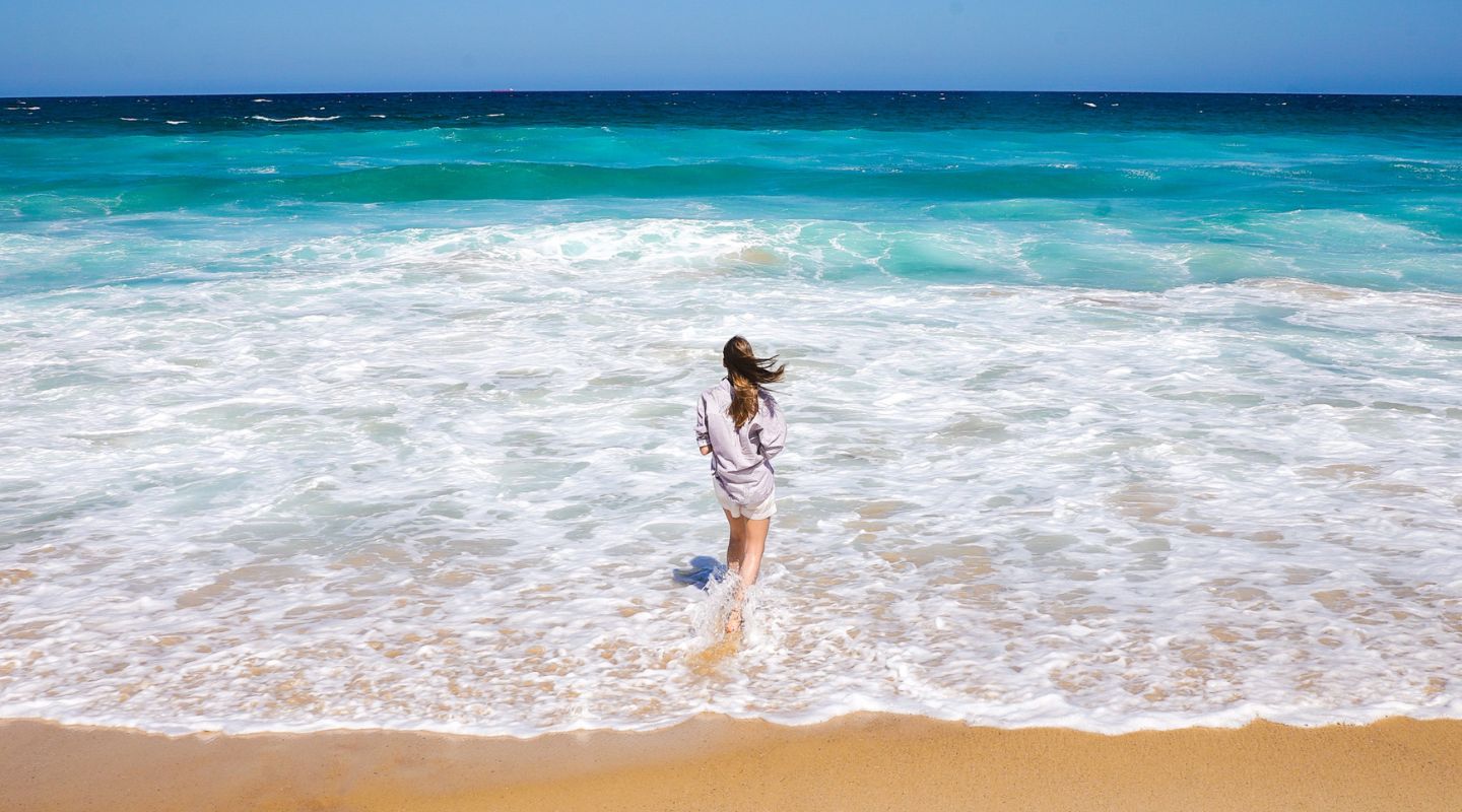 A woman stands on the shore as a wave washes around her feet