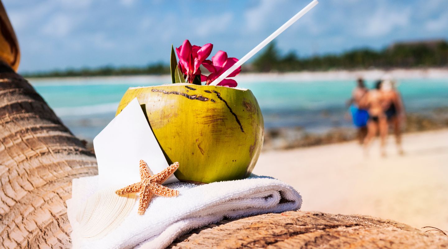 Coconut drink placed on a palm tree's trunk, with a view of the beach as background.