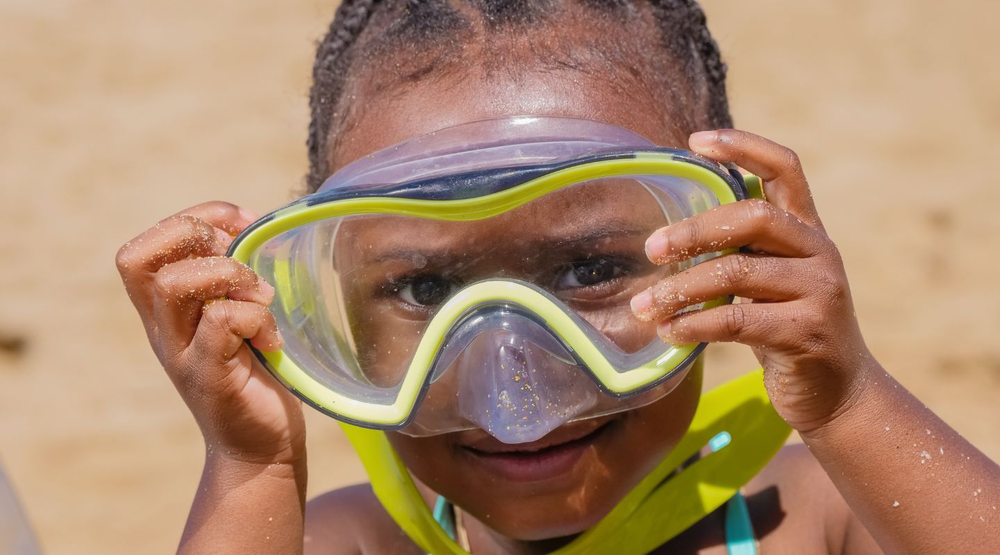 Small girl holding a snorkeling mask up to her face.