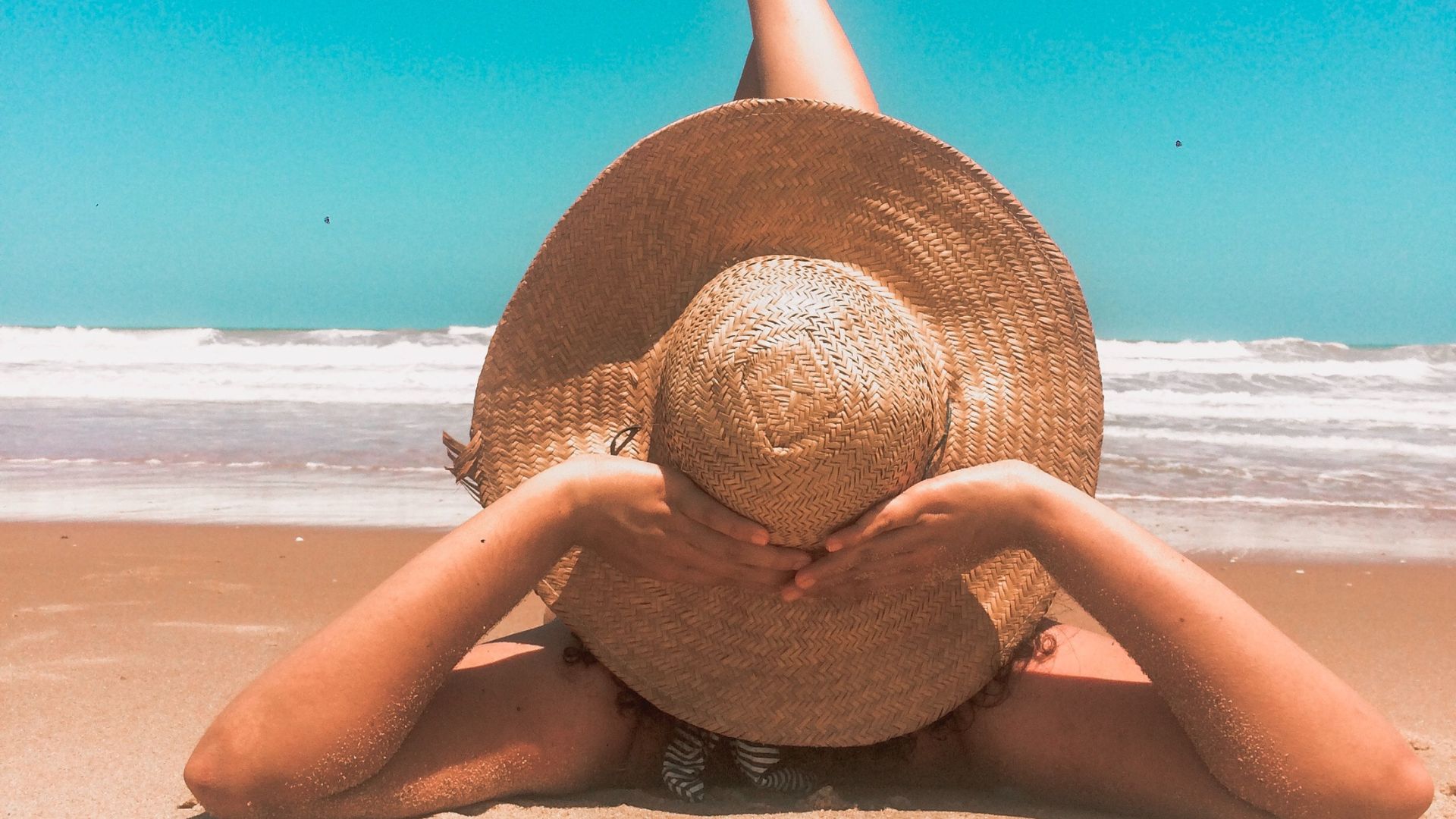 A woman wearing a large beach hat laying down in front of the sea