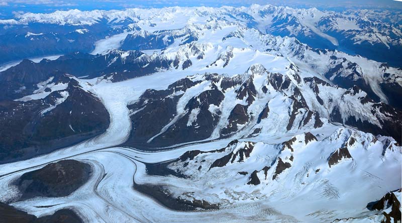 Several alpine glaciers converge in a large valley glacier. Notice the moraines (long black lines) from rock that was scraped off and transported by the moving ice.